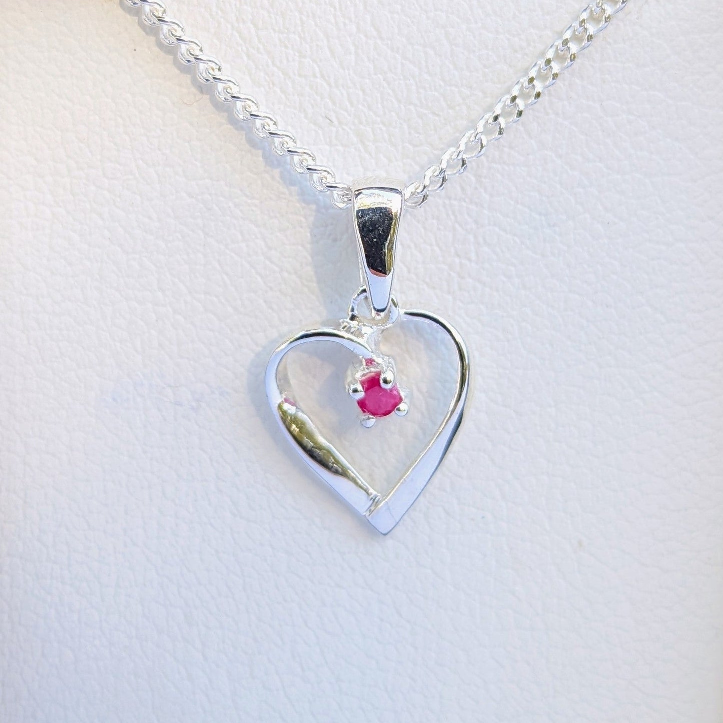 Heart-shaped silver pendant with a pink gemstone on a white background
